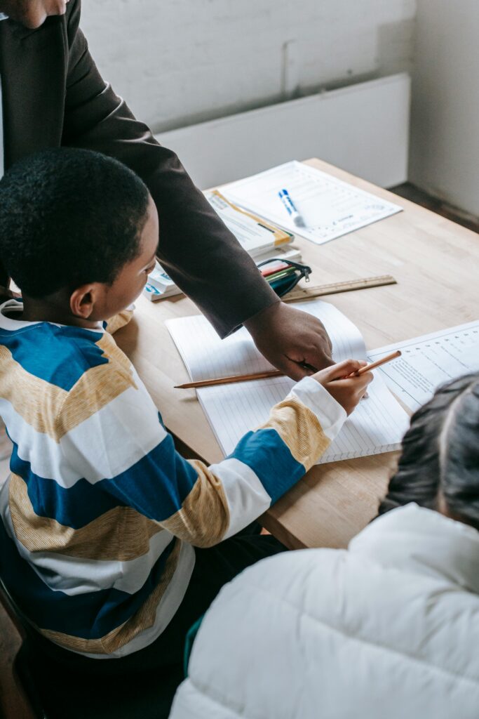 Educator helping children with schoolwork at a desk, promoting inclusive learning.